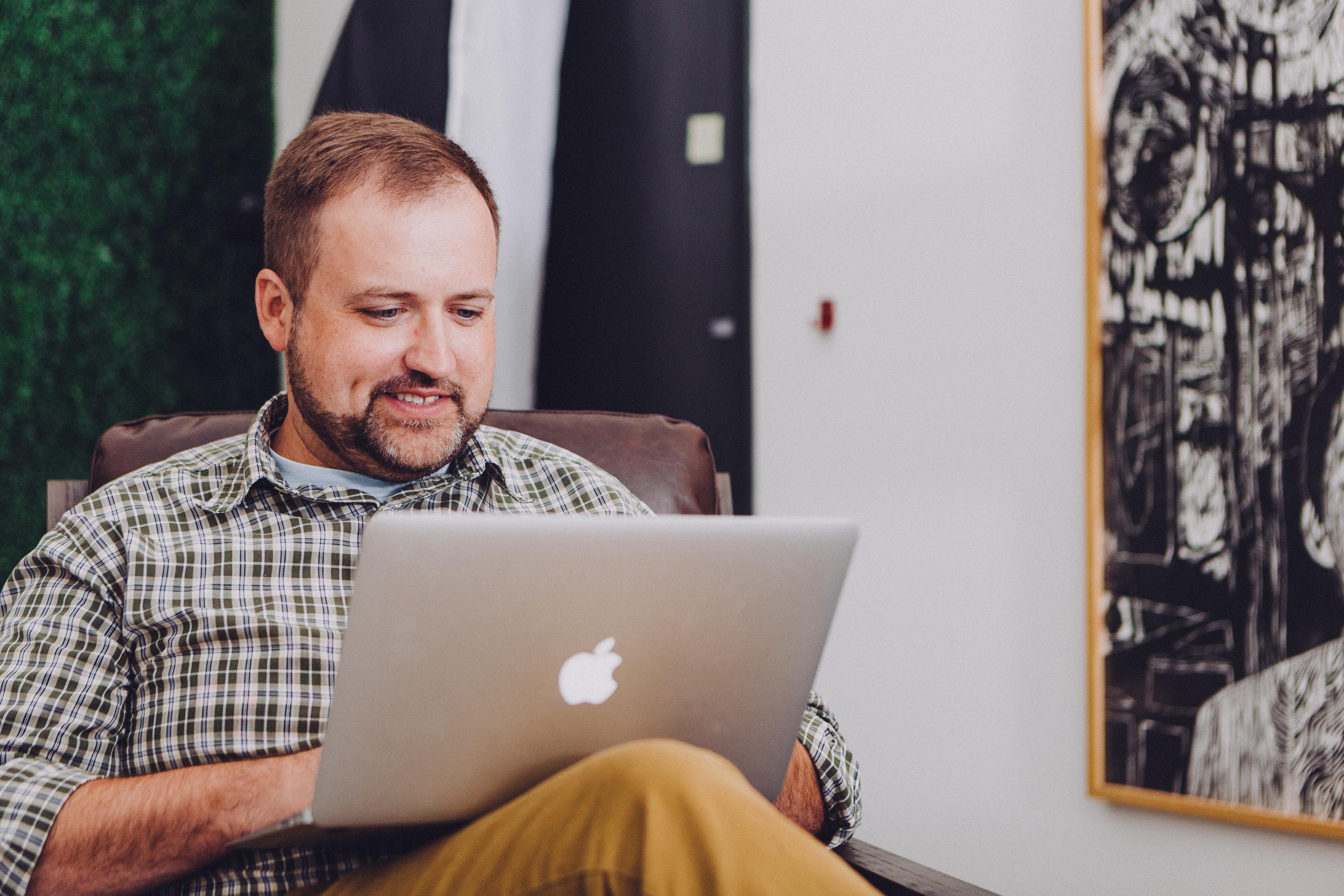 Man smiling using macbook on lap